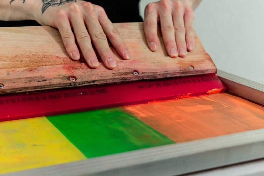 Holiday-Screenprinting-Design-Ideas-Unleash-Your-Festive-Spirit Hands using a squeegee for Austin screen printing on colorful fabric.